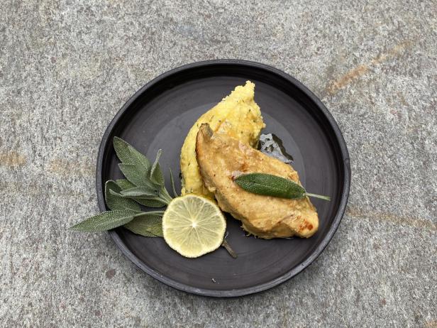 Ein Teller mit Huhn, Polenta, Zitrone und Salbe. 