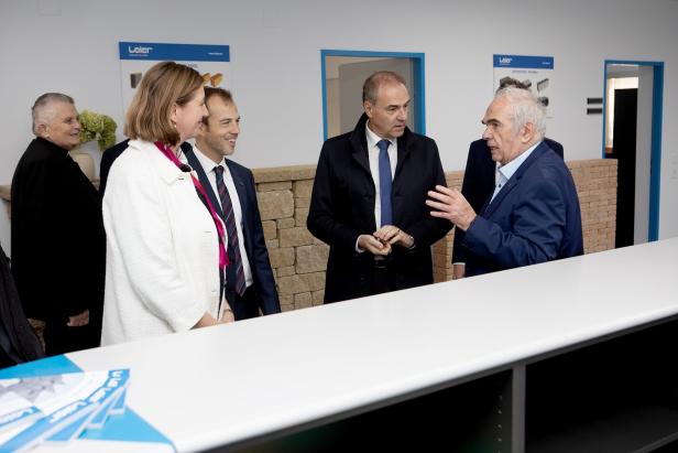 Eine Gruppe von Personen, darunter ein älterer Herr im blauen Anzug, unterhält sich in einem hellen Raum.