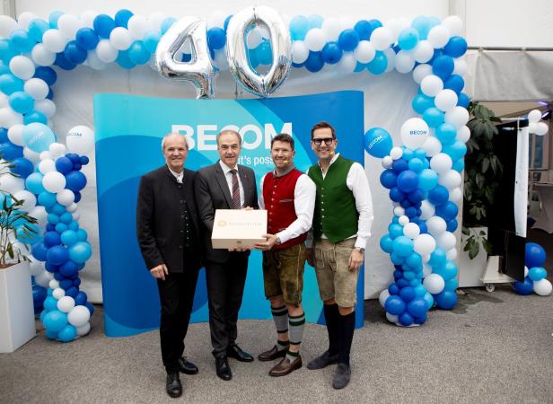 Vier Männer stehen vor einer blauen Ballon-Dekoration mit der Zahl 40, einer hält eine Geschenkbox.