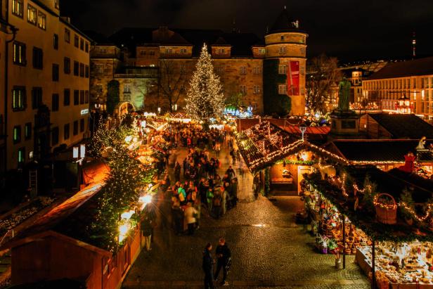 Weihnachtsmarkt bei Nacht mit beleuchtetem Weihnachtsbaum, Ständen und Menschen vor historischen Gebäuden.