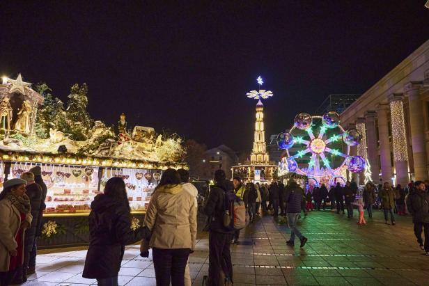 Weihnachtsmarkt bei Nacht mit beleuchteten Ständen, Karussell und Menschen auf gepflastertem Platz vor Gebäuden.