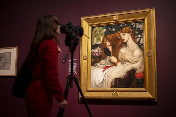 Eine Person fotografiert ein gerahmtes Gemälde einer rot haarigen Frau in einer Galerie.
