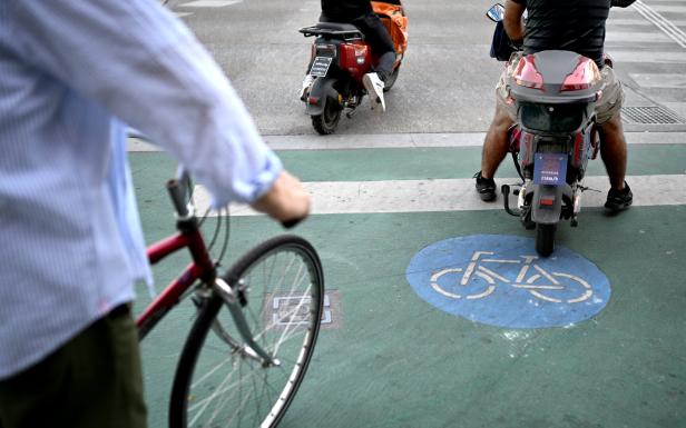 Ein Radfahrer und zwei Roller sind auf einem Radweg zu sehen.