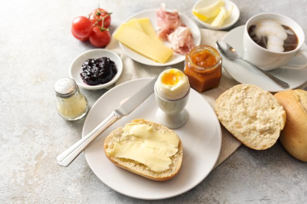 Breakfast with rolls, egg, jam, cheese and ham and a cup of coffee, light rustic background with copy space, selected focus