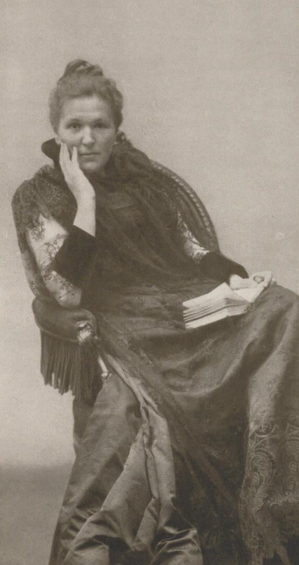 Eine Frau , Marie Lang, sitzt mit einem Buch in der Hand und stützt ihren Kopf ab.