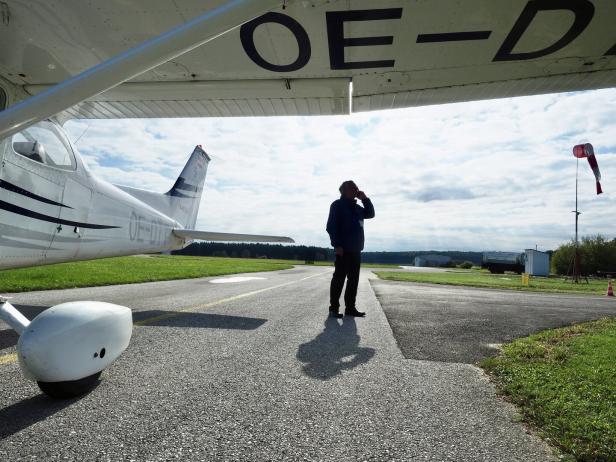 Ein Mann telefoniert auf einem Flugfeld neben einem Kleinflugzeug mit der Kennung OE-D**.