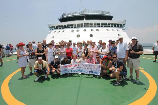 Eine Reisegruppe von Sagmeister-Reisen posiert vor einem Kreuzfahrtschiff mit einem Banner von kreuzfahrtprofi.at.