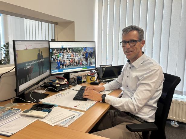 Ein Mann mit Brille sitzt an einem Schreibtisch vor zwei Monitoren und arbeitet am Computer in einem modernen Büro.