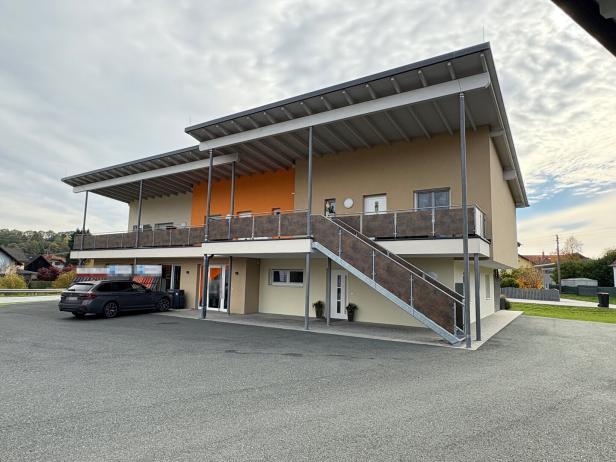 Modernes zweistöckiges Gebäude mit Außentreppe, überdachtem Balkon und geparktem Auto davor.