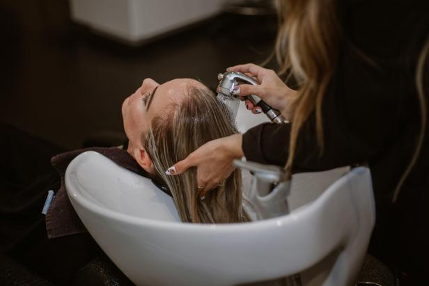 Eine Frau lässt sich im Salon die Haare waschen, während sie entspannt im Stuhl sitzt.