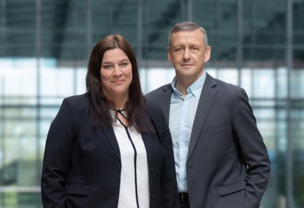 Zwei Personen in Businesskleidung stehen nebeneinander vor einem Glasgebäude. Zwei Personen in Businesskleidung stehen nebeneinander vor einem Glasgebäude.