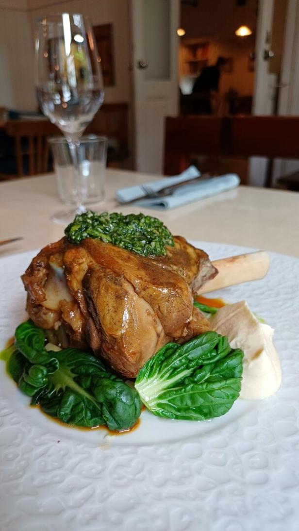  Geschmorte Lammstelze mit Süßerdäpfelcreme, Pak Choi, Gremolata, geschmortem Kürbis und Schalotten-Chutney serviert auf einem weißen Teller.