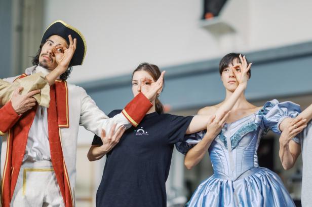 Zwei Frauen und ein Mann posieren auf einer Bühne in festlichen Kleidern für die Kamera.