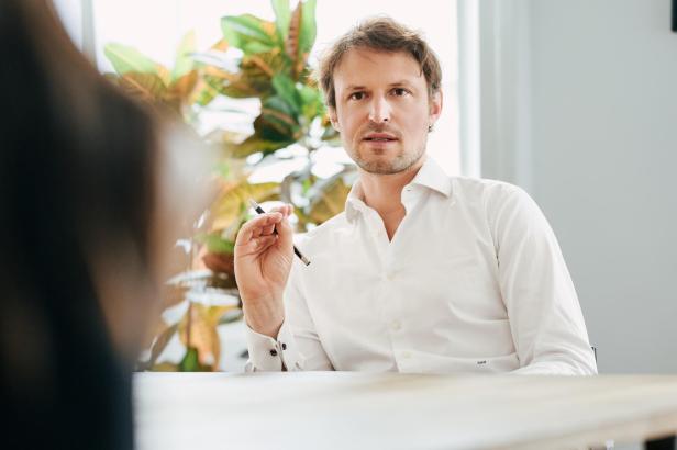 Mann in weißem Hemd sitzt an einem Tisch und hält einen Stift in der Hand.