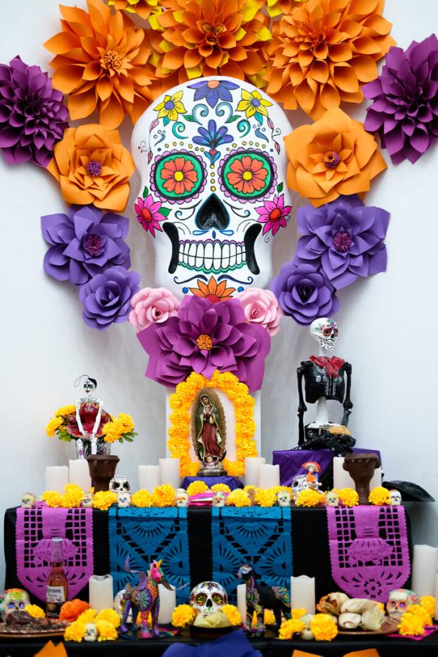 Bunt geschmückter Altar mit bemaltem Totenkopf, Papierblumen, Kerzen, Figuren und traditionellen Opfergaben.