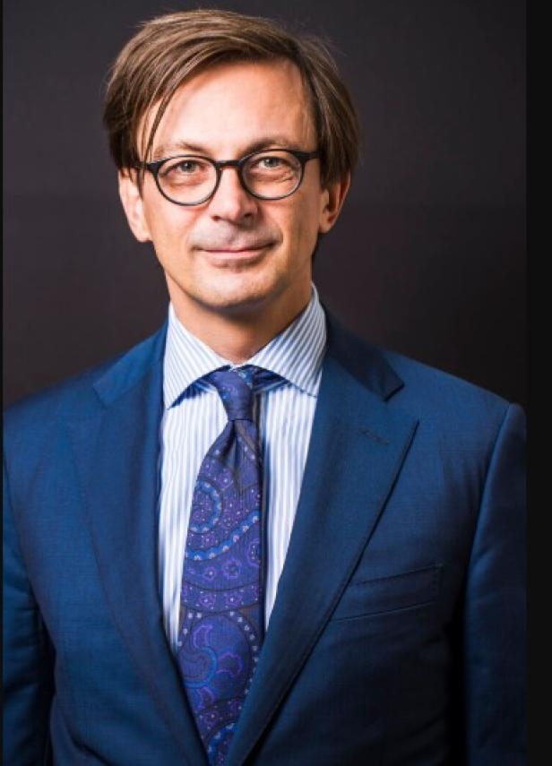 Michael Stampfer vom WWTF Ein Mann mit Brille, Anzug und Krawatte vor einem dunklen Hintergrund.