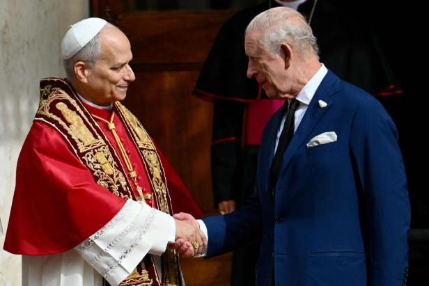 VATICAN-BRITAIN-ROYALS-POPE Der Papst in rotem Ornat und Charles im blauen Anzug geben sich die Hand und lächeln einander an.