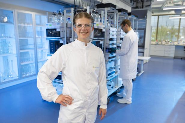 Zwei Personen in weißen Laborkitteln in einem Labor mit technischen Geräten und blauen Boden.