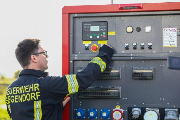 Ein Feuerwehrmann bedient ein großes Steuerpult mit zahlreichen Schaltern und Steckdosen im Freien.