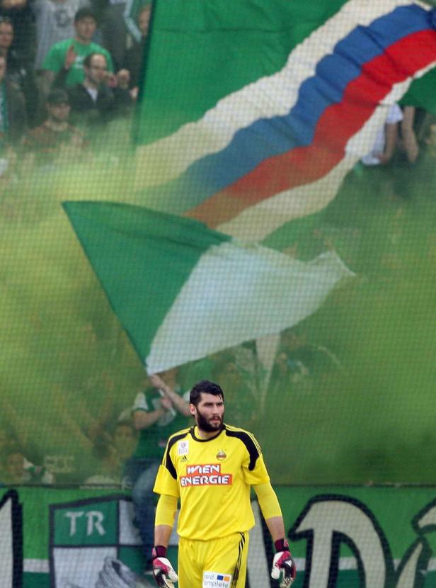 Ein Fußballtorwart in gelber Uniform steht vor einer Zuschauermenge mit Fahnen.