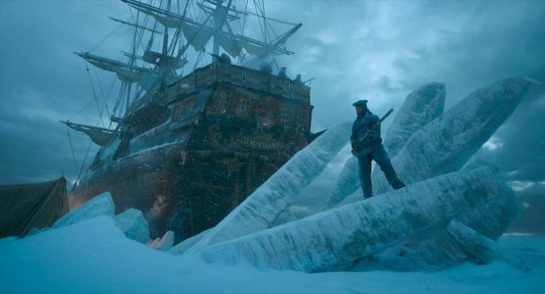 Eine Gestalt steht in einen verschneiten Eismeer. Ein Schiff dürfte darin eingefroren sein.