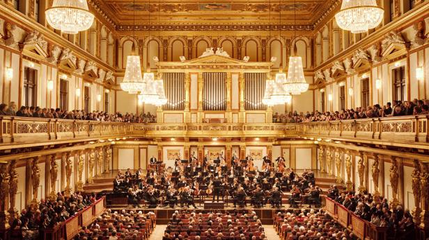 Großer Konzertsaal mit Orchester auf der Bühne und Publikum auf mehreren Ebenen unter prunkvollen Kronleuchtern.