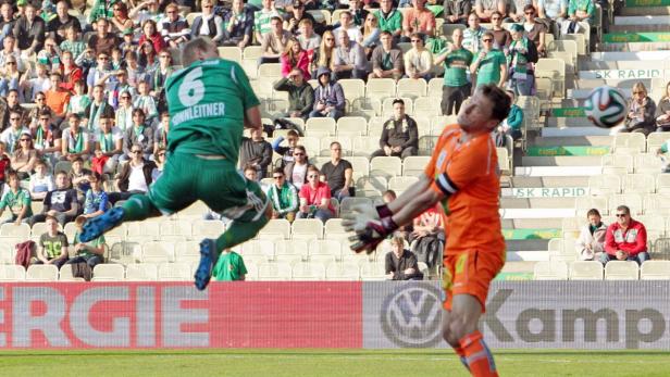 Ein Fußballspieler köpft den Ball vor dem Torwart und einer Zuschauertribüne.