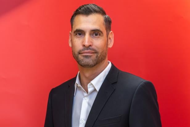 TIROL-LANDTAGSWAHL: LANDESPARTEIRAT SPÖ TIROL: SCHMID Ein Mann mit dunklem Haar und Bart trägt einen schwarzen Anzug und steht vor einem roten Hintergrund.