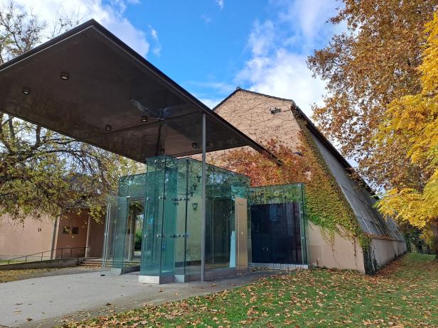 ++ THEMENBILD ++ KULTUR-COMEBACK IM ATELIER AUGARTEN Ein moderner gläserner Eingang mit großem Vordach führt zu einem von Efeu bewachsenen Gebäude im Herbst.