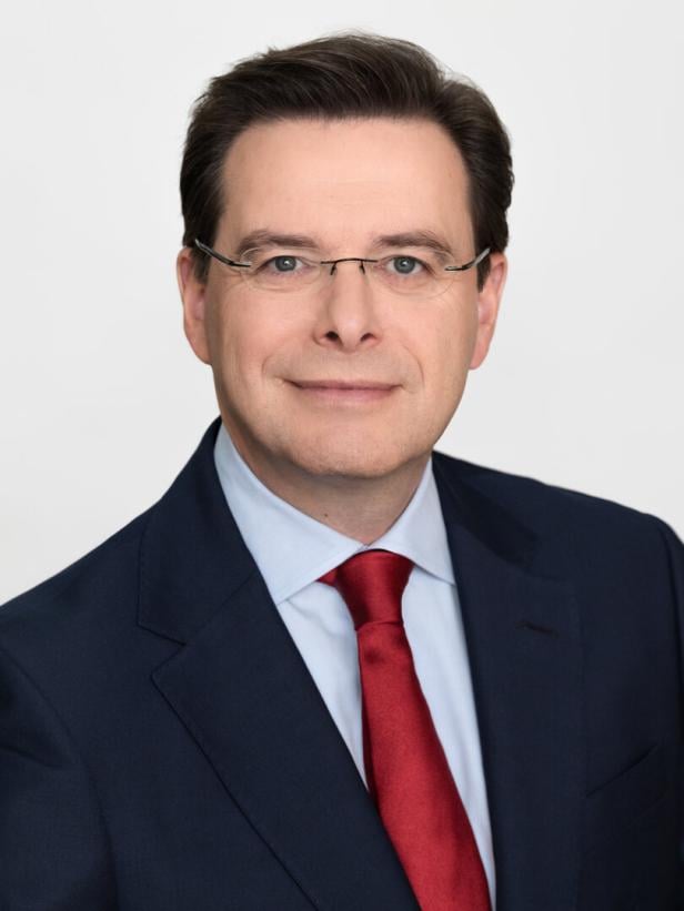 Mann mit braunen Haaren, Brille und Anzug lächelt in die Kamera