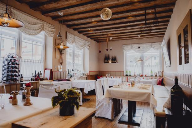 Ein helles Restaurant mit Holzbalkendecke und weiß gedeckten Tischen lädt zum Verweilen ein.