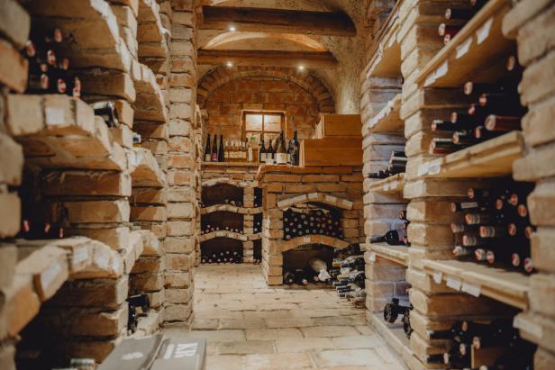 Ein Gewölbekeller mit Backsteinregalen, in denen zahlreiche Weinflaschen gelagert werden.
