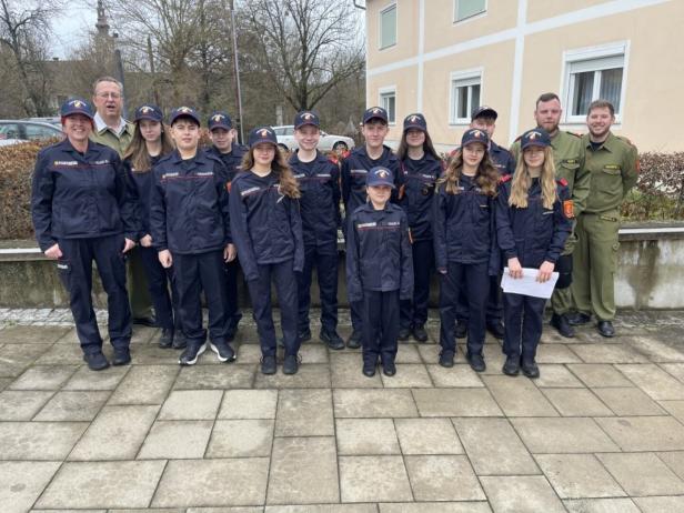 Eine Gruppe von Jugendlichen und Erwachsenen in Feuerwehruniformen steht draußen vor einem Gebäude und lächelt in die Kamera.