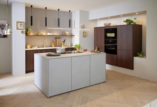 Moderne Küche mit Kücheninsel in hellgrau, dunklen Holzschränken, eingebauten Backöfen und Pendelleuchten über der Arbeitsfläche.