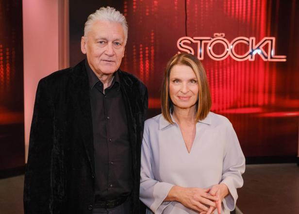 Rainhard Fendrich und Barbara Stöckl stehen gemeinsam im Studio der ORF-Talkshow „Stöckl“ vor dem leuchtenden Sendungslogo.