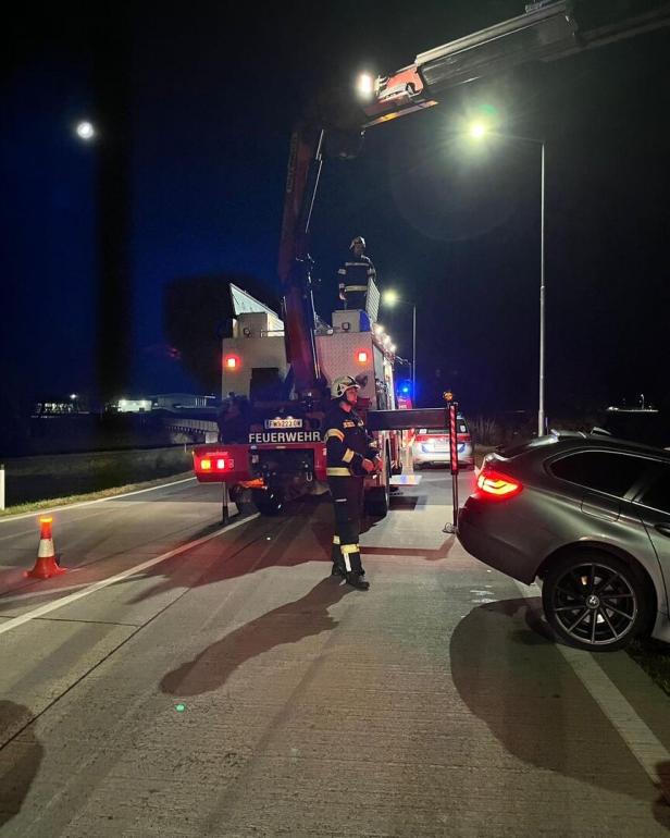 Feuerwehrleute sichern nachts eine Unfallstelle mit einem Kran und einem beschädigten Auto auf der Straße.
