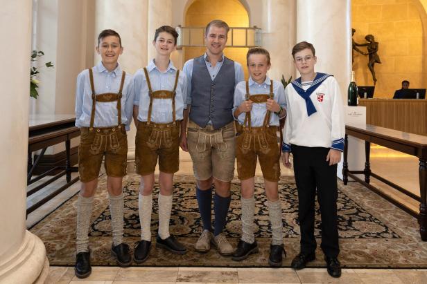 Drei Buben und ein Mann in Lederhosen, ein Bub in Sängerknaben-Montur in einer Hotellobby