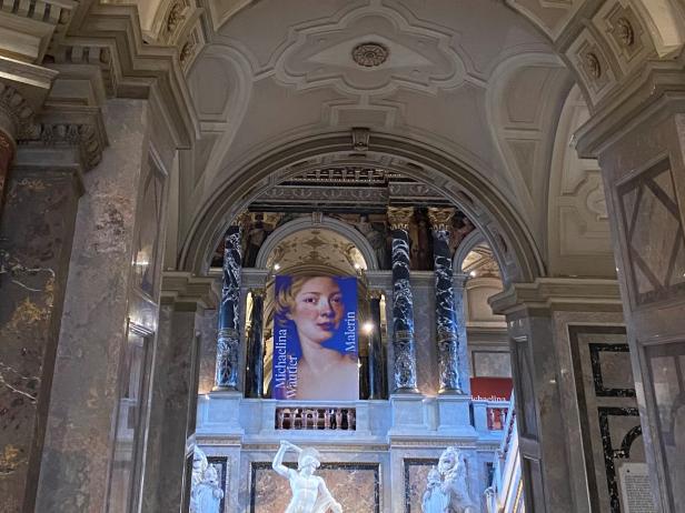 Großer, prunkvoller Innenraum mit gewölbter Decke, verzierten Säulen und einem Banner mit blauem Hintergrund und weißer Schrift.