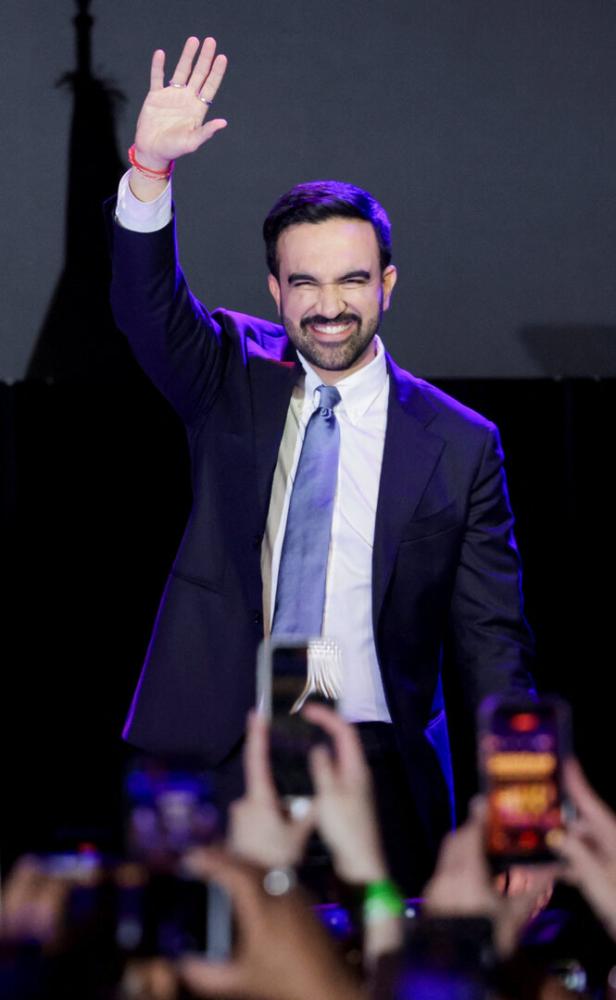 Ein Mann im Anzug winkt lächelnd einer jubelnden Menschenmenge zu.