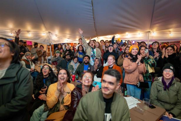 Viele Menschen unter einem Zelt jubeln, lachen und klatschen, während sie gemeinsam etwas verfolgen.