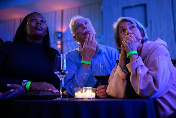 Drei Menschen sitzen an einem Tisch mit Kerzen und Getränken und schauen nachdenklich in dieselbe Richtung.