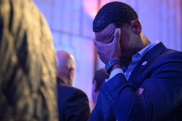 Ein Mann im Anzug hält sich mit der Hand das Gesicht und wirkt emotional betroffen.