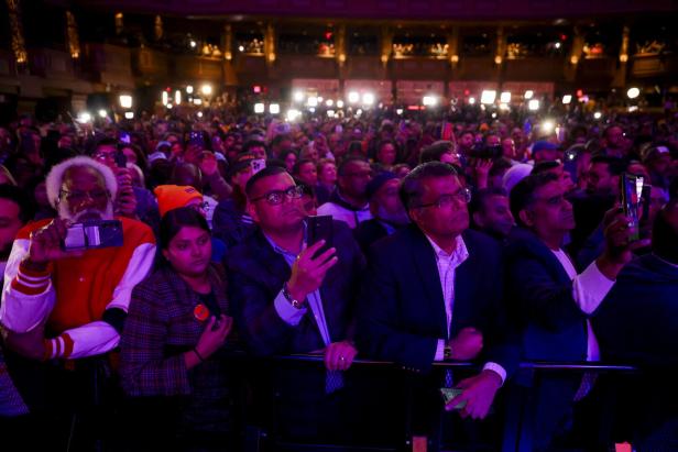 Viele Menschen stehen dicht gedrängt in einer Halle, viele halten ihre Handys hoch und schauen gespannt nach vorne.