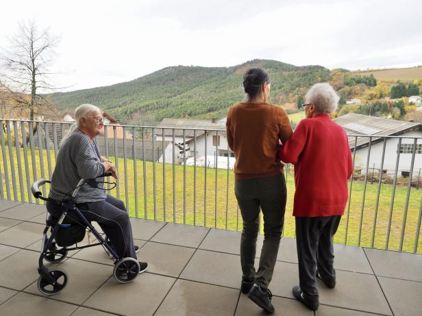 Drei Menschen, darunter zwei ältere Frauen und eine jüngere Person, blicken gemeinsam auf eine grüne Hügellandschaft.