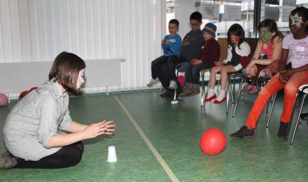 Eine Frau mit weißer Gesichtsbemalung führt einen Zaubertrick vor einer Gruppe von Kindern auf.