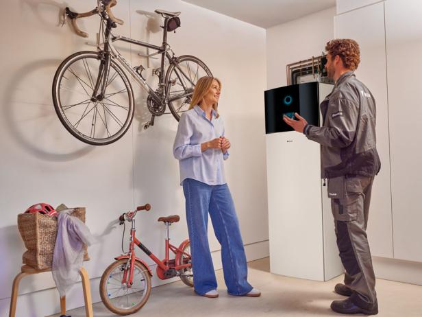 Eine Frau und ein Mann stehen bei einem Innengerät einer Wärmepumpe.