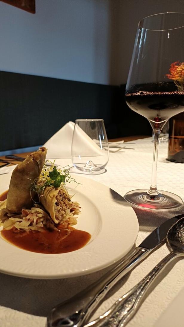 Röllchen mit Gänsefleisch gefüllt stehen auf einem Tisch beim Jungwirt. Daneben ein Glas Wein.