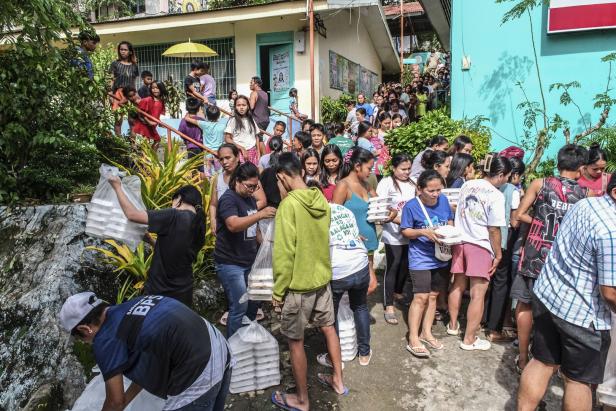 Viele Menschen stehen in einer Schlange im Freien, um Essenspakete zu erhalten, die von Helfern verteilt werden.