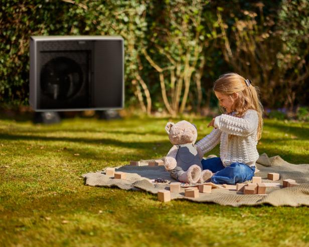 Ein Mädchen sitzt auf einer Spieldecke im Garten auf dem Grad und spielt mit ihrem Teddybär.
