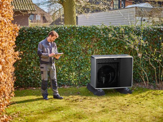 Ein Mann steht im Garten neben dem Außengerät einer Wärmepumpe.
